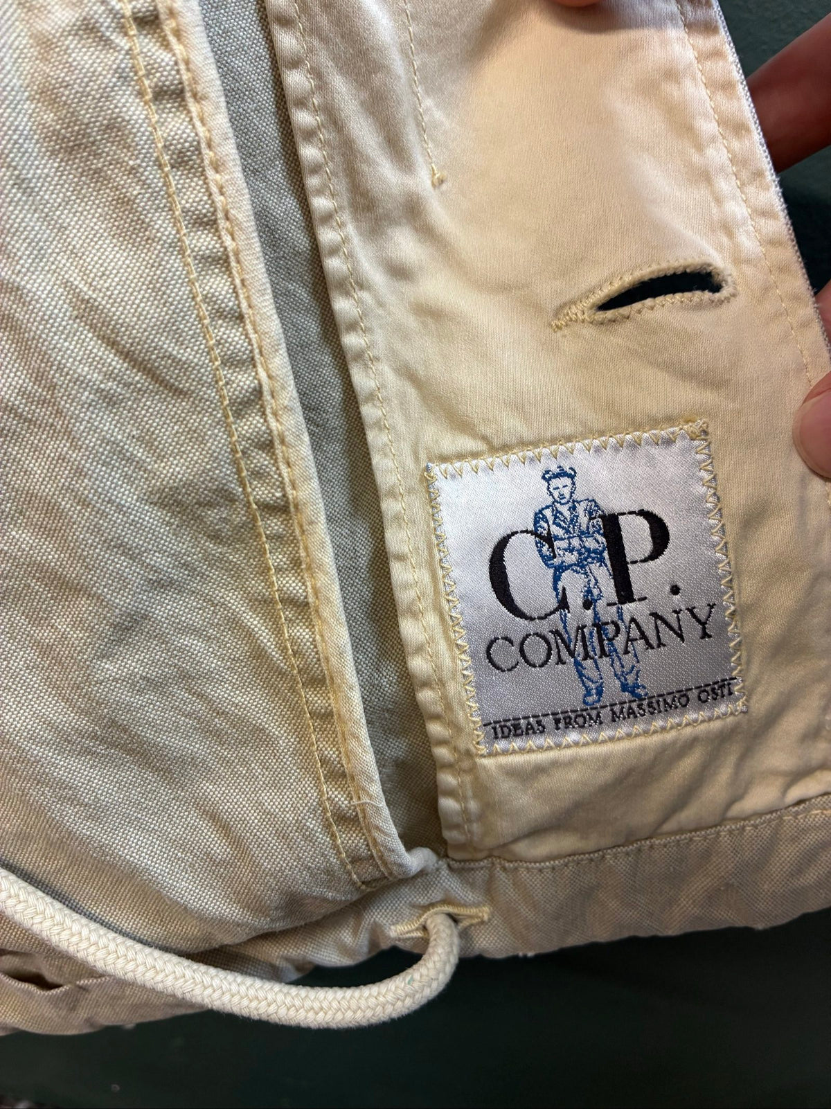 C.P. Company beige cotton field jacket with mild distress and green paint marks.