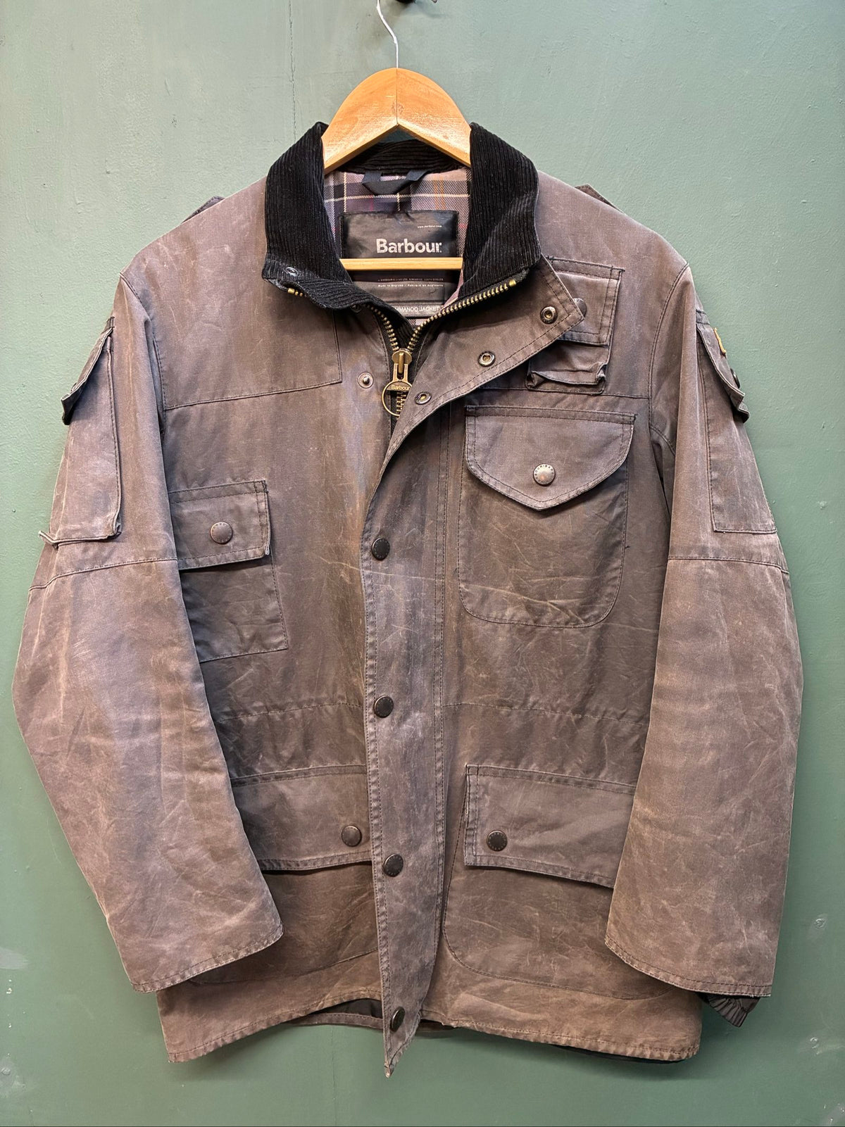 Barbour black and grey wax jacket with military utility design and made in England tag.