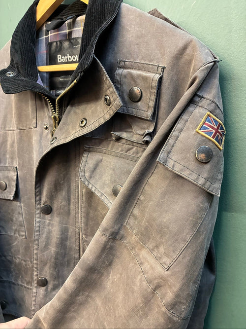 Barbour black and grey wax jacket with military utility design and made in England tag.