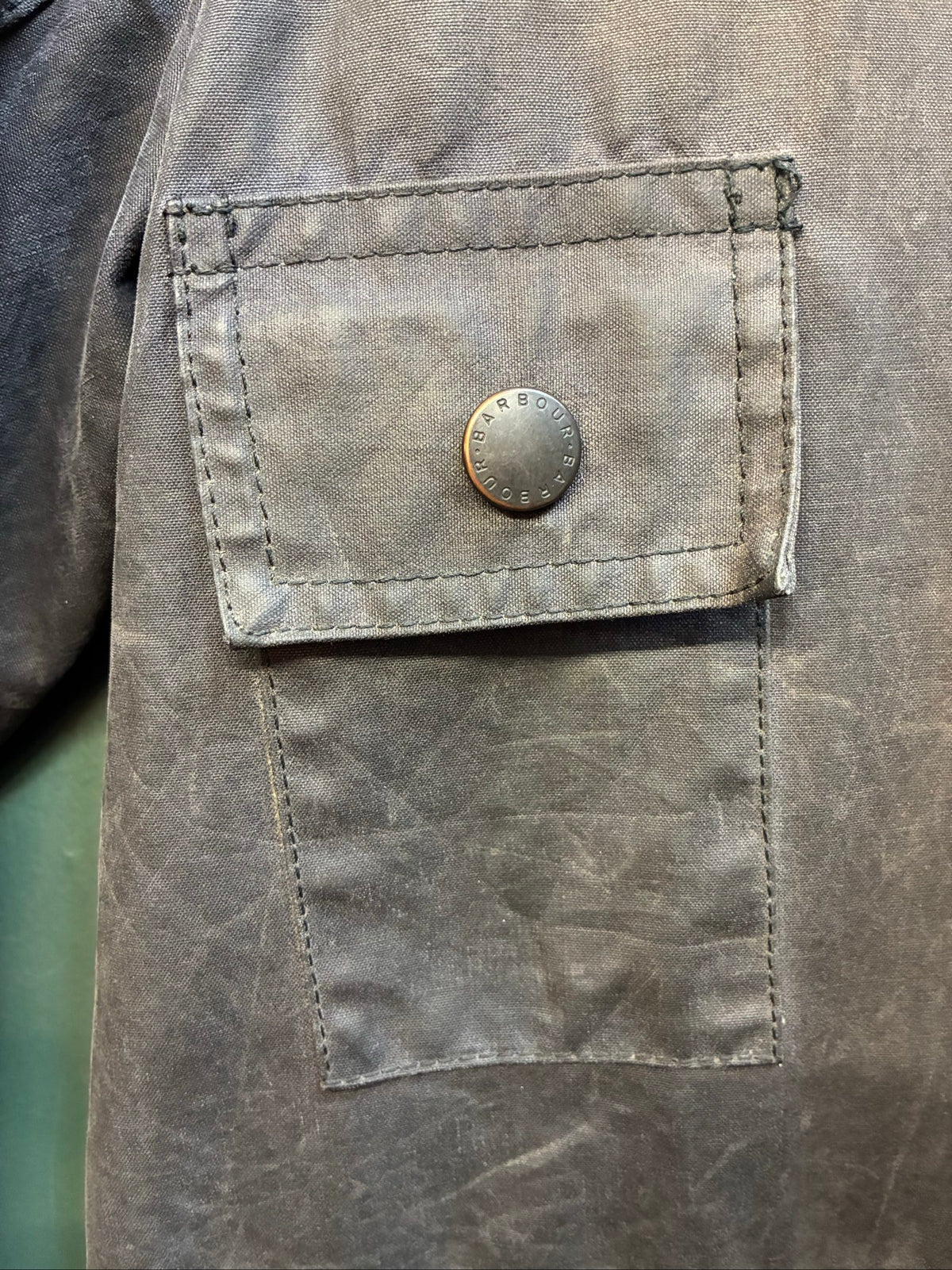 Barbour black and grey wax jacket with military utility design and made in England tag.